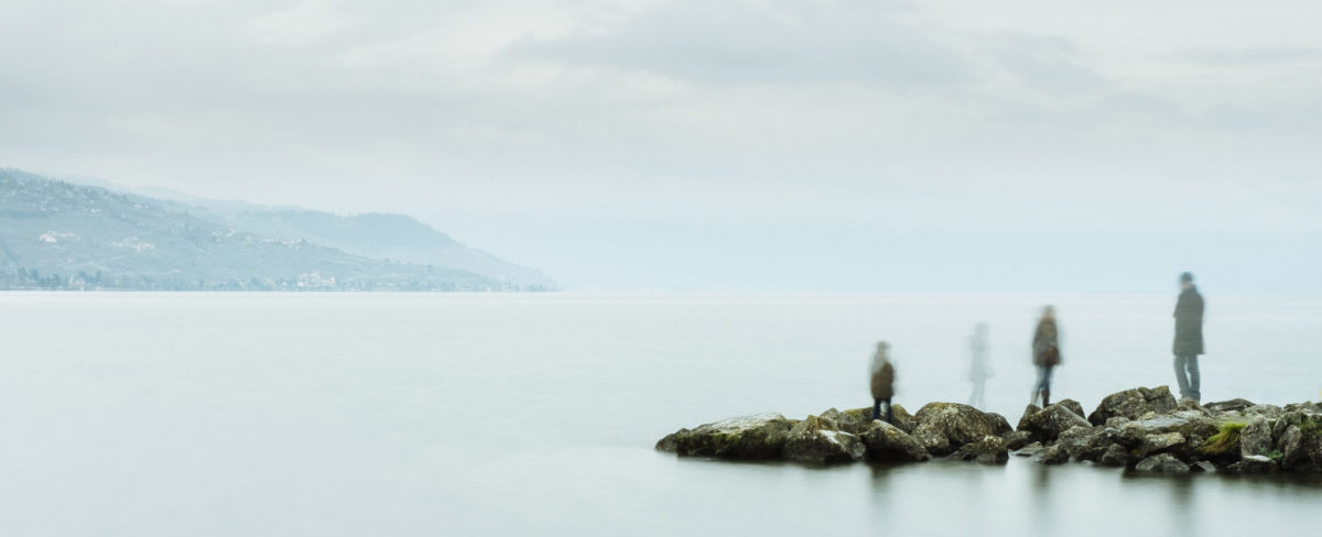 Four fading people standing on a rock bar into a lake